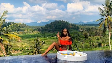 A person relaxing on a poolside with a view of a lush landscape and mountains in the background.