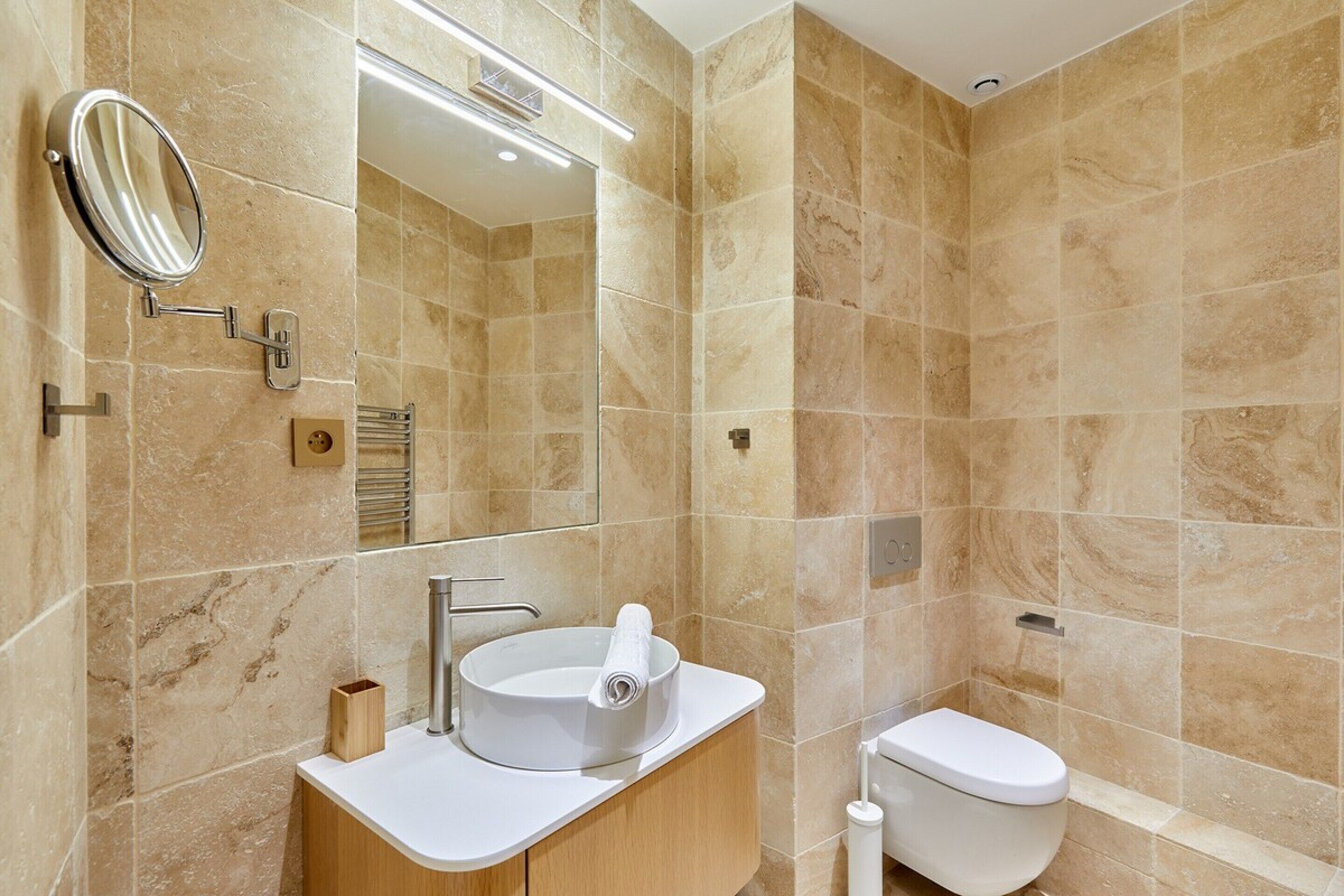 Une salle de bain moderne avec des carreaux de marbre beige, un lavabo blanc avec un miroir et des toilettes.