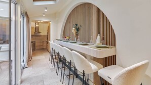 A modern dining area with a long table, white chairs, and a wooden accent wall. - Terrace Apartment Trocadero Eiffel Tower (Paris)