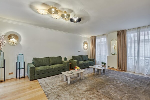 Un salon moderne avec deux canapés verts, une table basse en bois et un grand tapis.