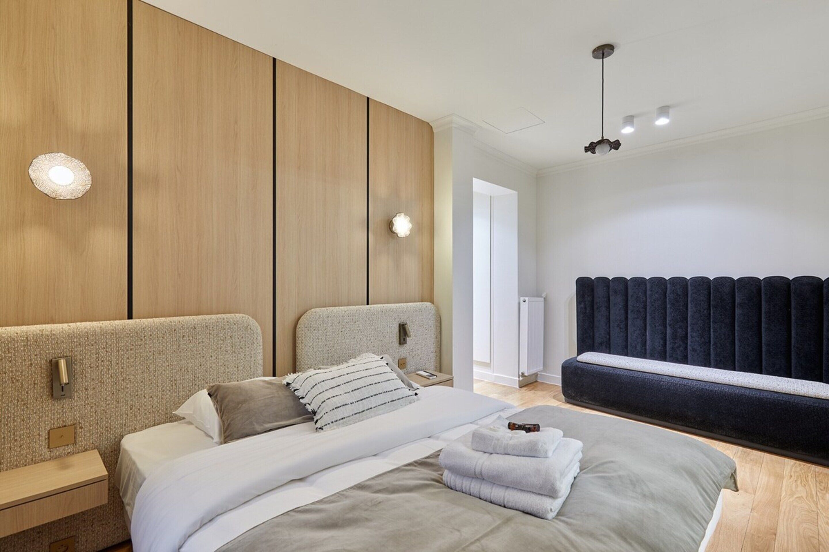 A modern bedroom with a large bed, a bedside table, a wardrobe, and a bench.