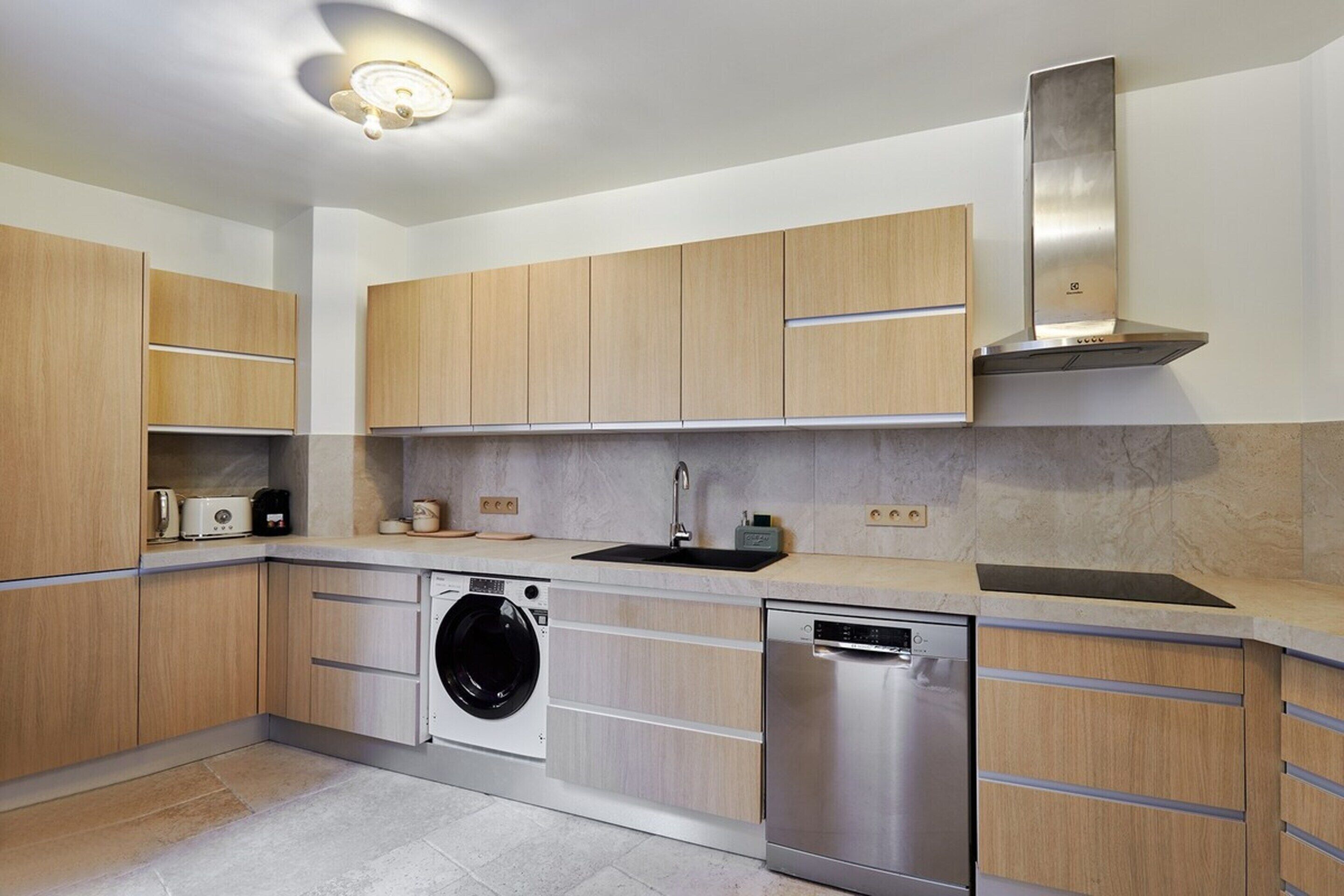 A modern kitchen with wooden cabinets, a built-in washing machine, a dishwasher, and a stainless steel range hood.