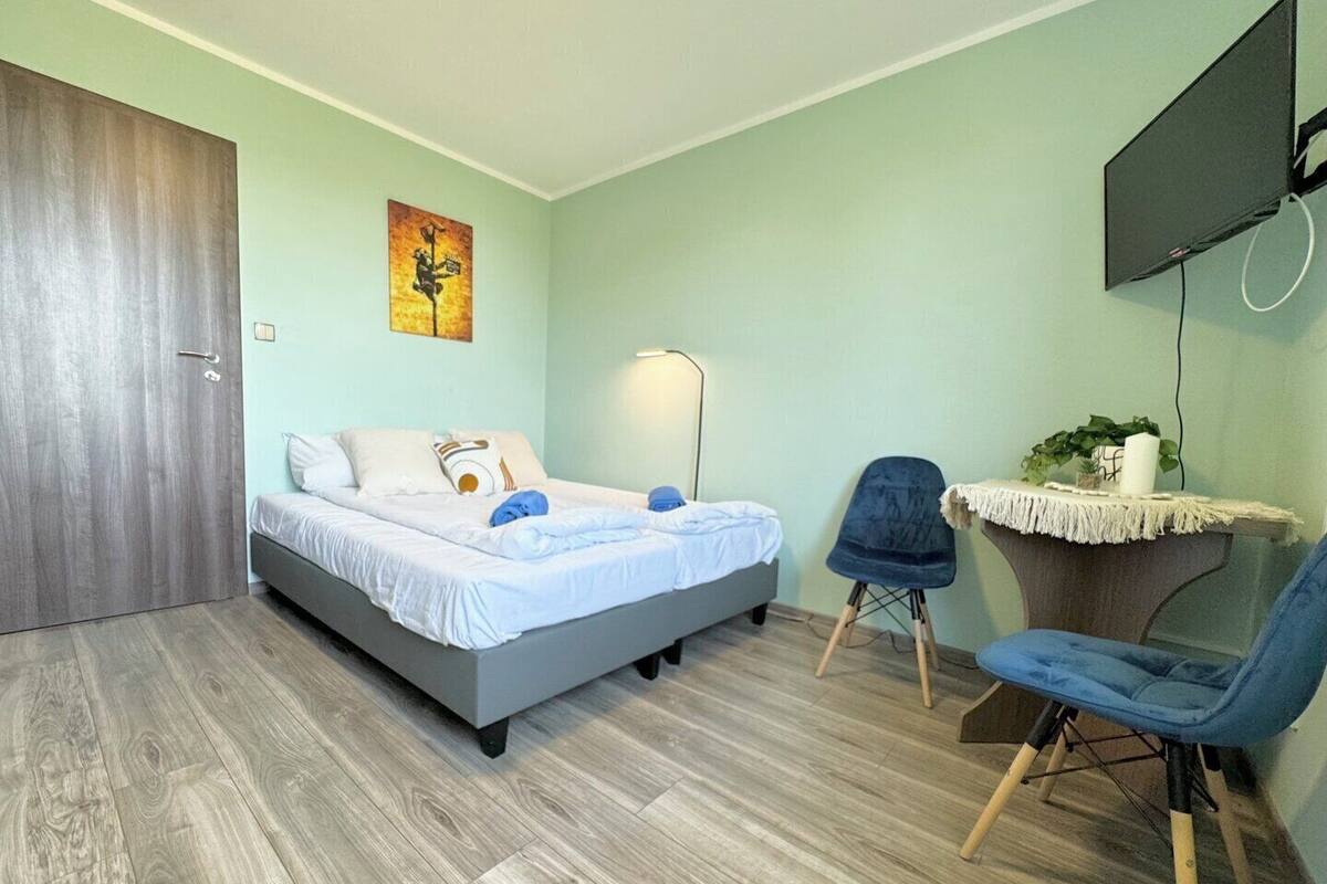 A bedroom with a bed, a desk, a chair, a TV, and a painting on the wall.