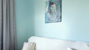 A room with a light blue wall, a white textured sofa, and a beige pillow. - Pensjonat Błękitna Przystań (Puck)