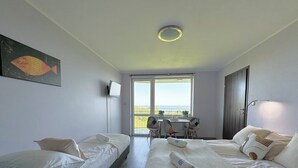 A hotel room with two single beds, a large bed, a TV, a balcony with a table and chairs, and a view of the sea. - Pensjonat Błękitna Przystań (Puck)