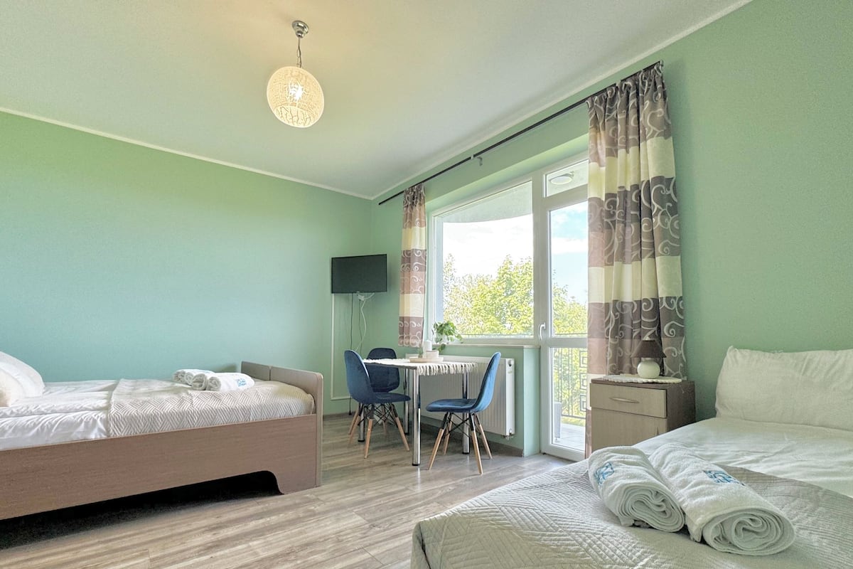 A hotel room with two beds, a desk with a chair, a TV, and a window with curtains.