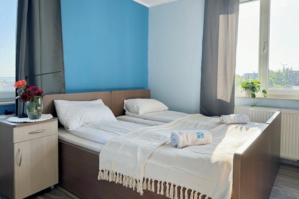 A hotel room with a bed, a bedside table, a window with curtains, and a view of the cityscape.