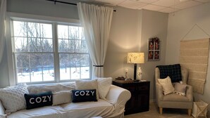 A cozy living room with a large window, a sofa with decorative pillows, a side table with a lamp, a chair, and a patterned rug. - Cozy SAFE 1 BR Private apartment Traveling Professionals near skiing Hospitals (Exeter)
