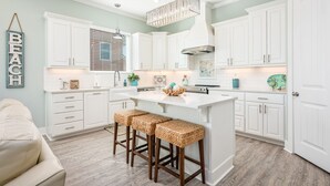 A modern kitchen with white cabinetry, a central island with stools, and a hanging light fixture. - Crystal Breeze - beautiful 3 bdrm, with gulf view - just steps to the beach! (Crystal Beach)