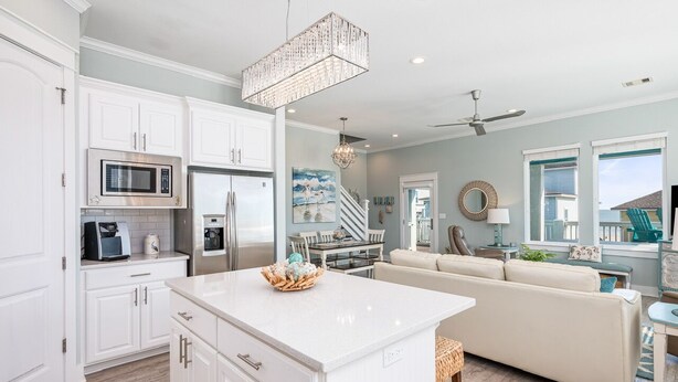 A modern kitchen with white cabinetry, a central island, and a dining area with a sofa and table. - Crystal Breeze - beautiful 3 bdrm, with gulf view - just steps to the beach! (Crystal Beach)