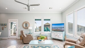 A living room with a ceiling fan, a television, a beach-themed rug, and a view of the beach through the windows. - Crystal Breeze - beautiful 3 bdrm, with gulf view - just steps to the beach! (Crystal Beach)