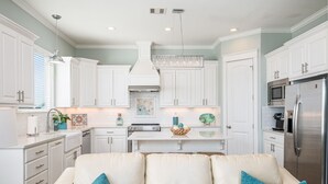 A modern kitchen with white cabinetry, a stainless steel refrigerator, and a central island. - Crystal Breeze - beautiful 3 bdrm, with gulf view - just steps to the beach! (Crystal Beach)