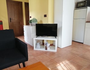 Un salon comprenant un téléviseur posé sur un meuble, un canapé, une petite table, un buffet et un coin cuisine avec un four à micro-ondes.