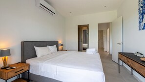 Ein modernes Hotelzimmer mit einem großen Bett, Nachttischen, einer Klimaanlage und einem Schreibtisch mit einer Lampe.