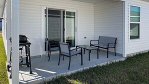 A covered patio area with a table and chairs, a grill, and a sliding glass door. - Cozy Retreat Near Sawgrass Market & Brownwood Paddock Square! (Wildwood)