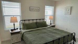 A bedroom with a metal bed frame, green bedding, two bedside lamps, and a wall with a bird painting and a 'JOY in the JOURNEY' sign. - Cozy Retreat Near Sawgrass Market & Brownwood Paddock Square! (Wildwood)
