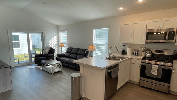 A modern kitchen with a central island, stainless steel appliances, and a dining area with a sofa and coffee table. - Cozy Retreat Near Sawgrass Market & Brownwood Paddock Square! (Wildwood)