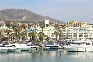A marina with boats docked, palm trees, and buildings in the background. - Charming House by the Sea (Benalmádena, Urbanización Benalgolf)