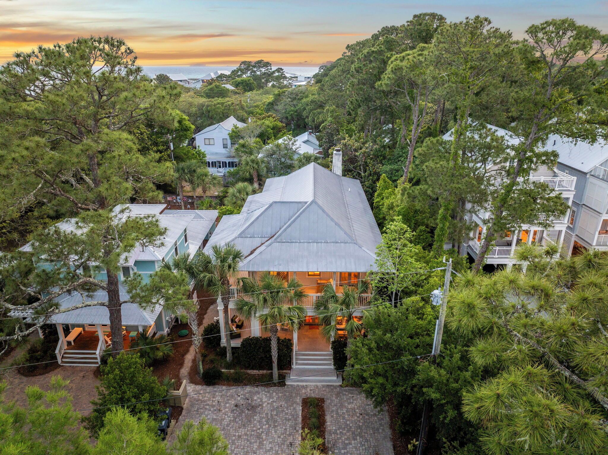A coastal house with a prominent gabled roof, surrounded by dense greenery and other residential buildings.