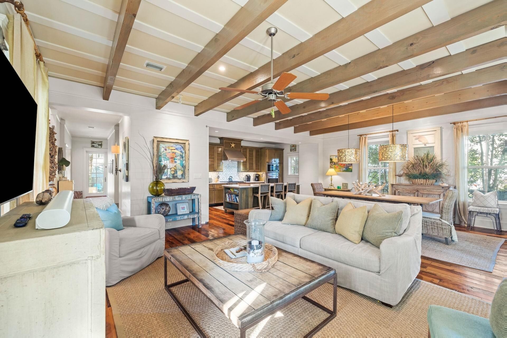 A spacious living room with a wooden ceiling, a large sofa, a coffee table, and a kitchen in the background.