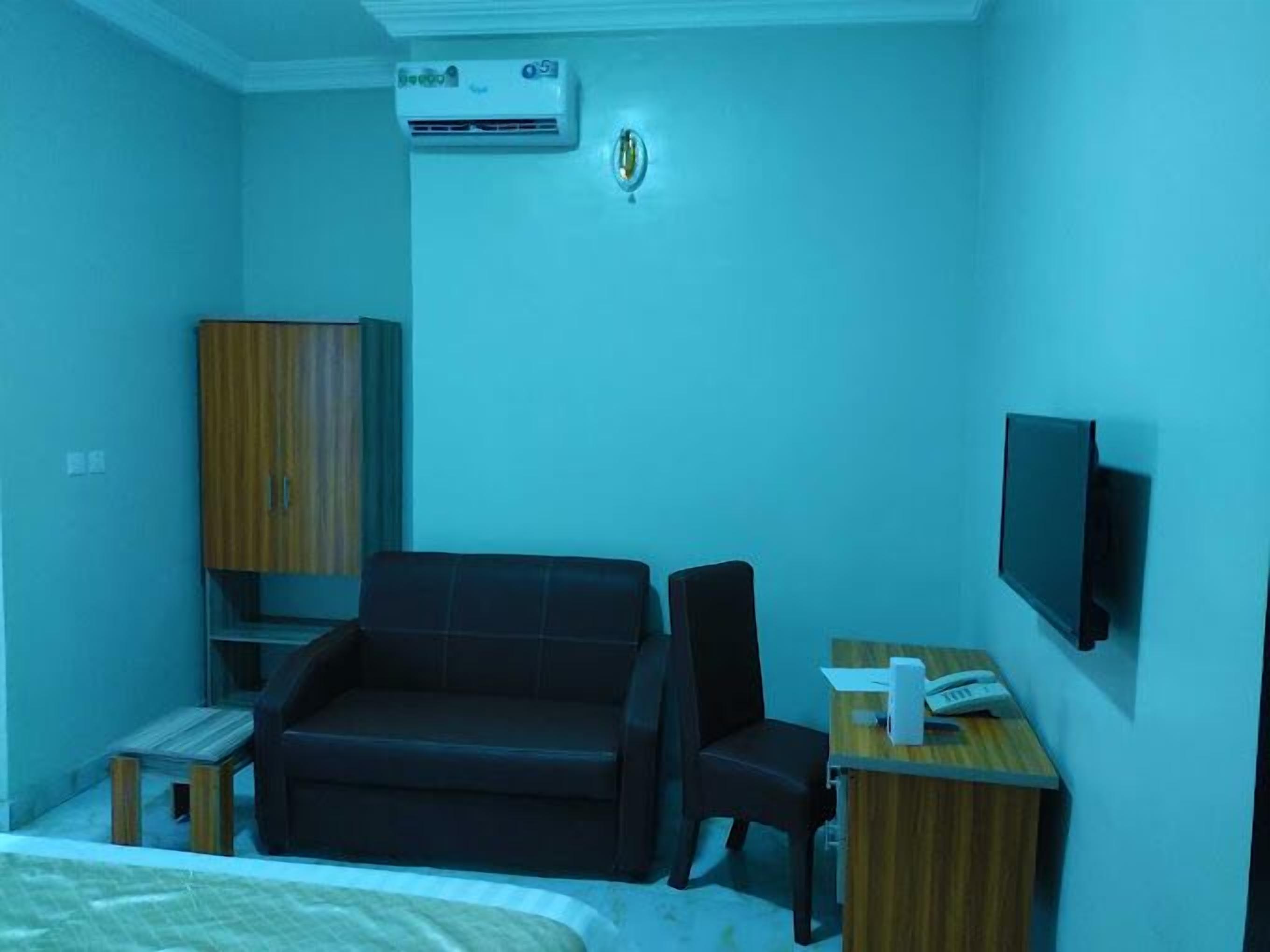 A hotel room with a bed, a sofa, a desk with a telephone, and a TV mounted on the wall.