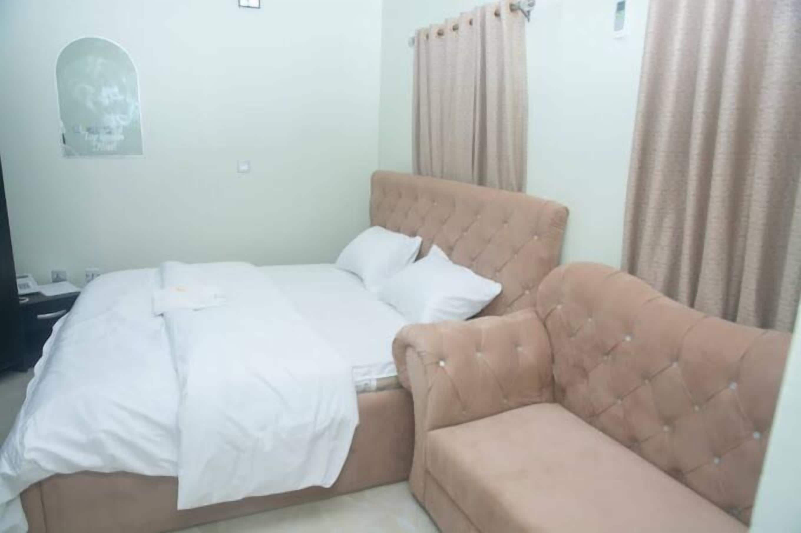 A bedroom with a bed, a sofa, a wall-mounted light, and a window with curtains.