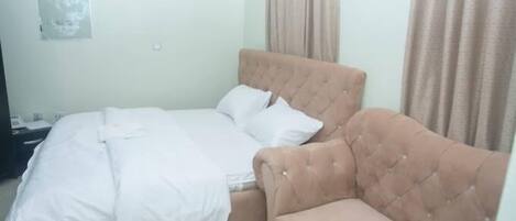A bedroom with a bed, a sofa, a wall-mounted light, and a window with curtains.
