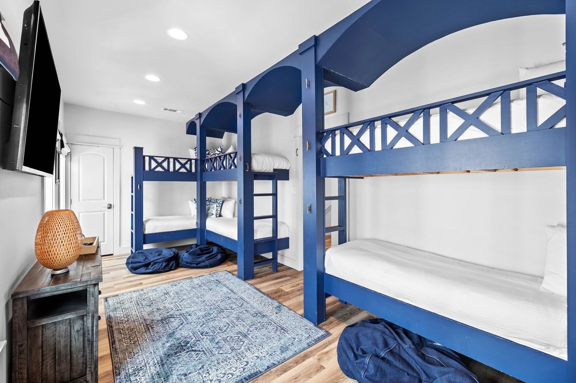 Um quarto com beliches, um armário de madeira, um tapete estampado e uma televisão na parede.