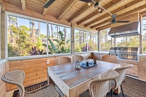 Enjoy al fresco dining in this serene outdoor space with a wooden table and six chairs, surrounded by large windows offering a view of the forest.