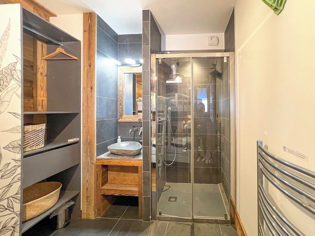 Ein modernes Badezimmer mit einer Duschkabine aus Glas, einem Holzwaschtisch und einem großen Spiegel.