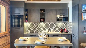 A modern kitchen with dark cabinetry, a patterned backsplash, and a wooden ceiling. - Apartment Lumikki |  Private hot tub and sauna (Les Gets)