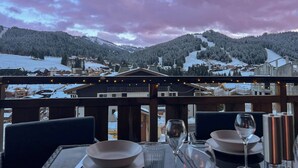 A restaurant with a view of a snow-covered mountain range and a town below. - Apartment Lumikki |  Private hot tub and sauna (Les Gets)