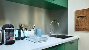 Una cucina moderna con un piano di lavoro bianco, mobili verdi e un lavello in acciaio inossidabile. Sul piano si trovano una macchina da caffè, un bollitore e un espositore per piatti. Un'espressione motivazionale è esposta sulla parete.