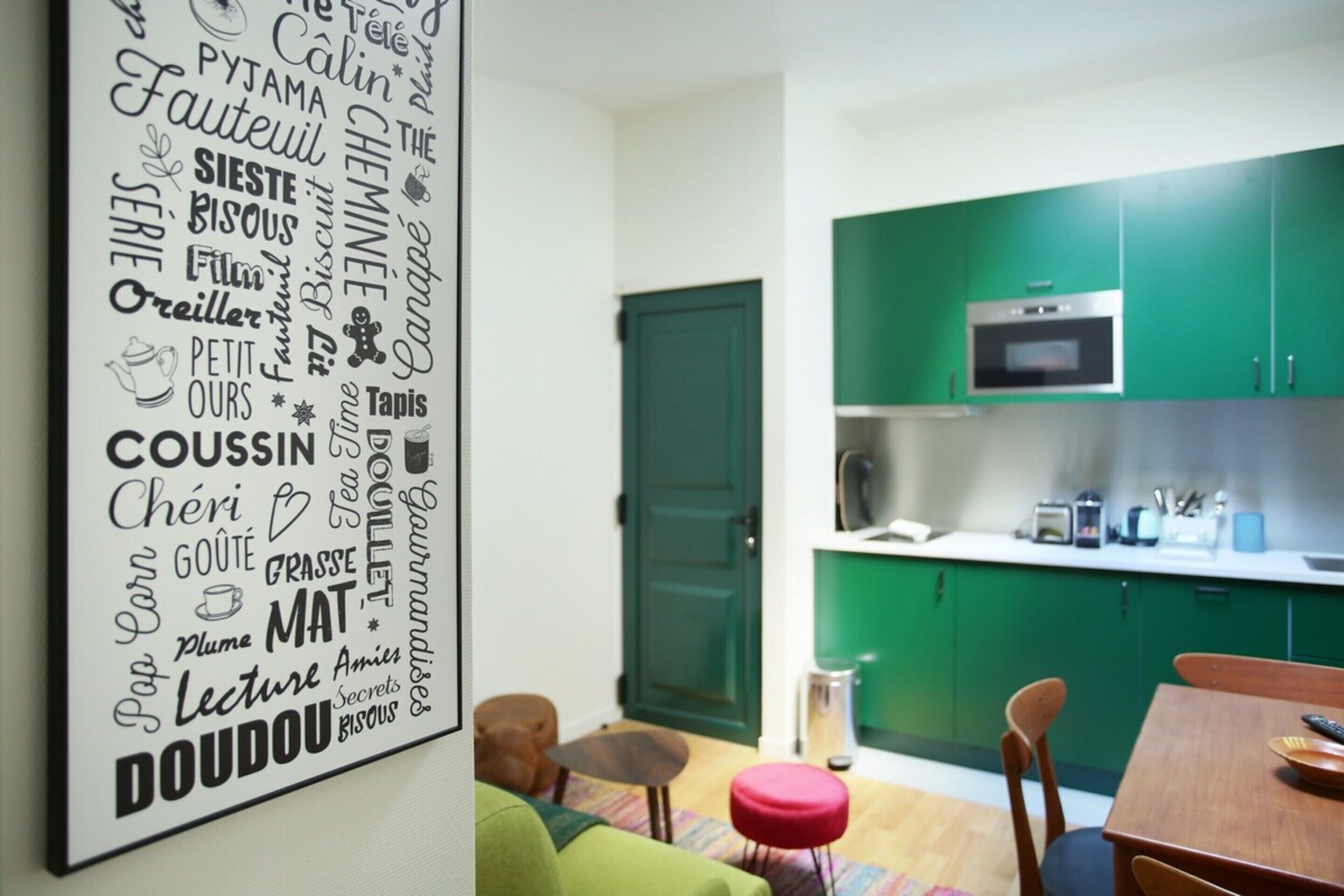 A modern kitchen with green cabinets, a microwave, and a small dining area with a table and chairs.