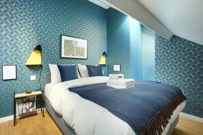 A bedroom with a large bed, two bedside lamps, a framed artwork, and a small table with a bowl and a sign. - Sublim and New Duplex Le Marais/beaubourg (Paris)