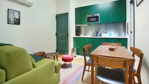 Un ambiente compatto con angolo cottura, zona pranzo e divano verde.
