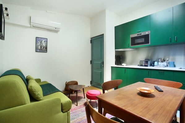 A compact living space with a green sofa, a wooden dining table, and a kitchenette with green cabinets. - Sublim and New Duplex Le Marais/beaubourg (Paris)