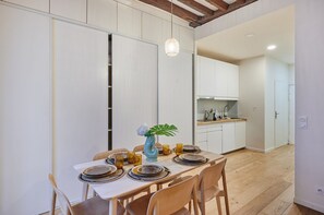 A dining area with a table set for four, a vase with a plant, and a kitchen in the background. - Sublim Apartement Saint Germain des Pres (Paris)