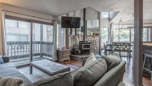 A spacious living area with a stone fireplace, a television, and a balcony with a view of the outside.