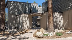 A modern building with a covered entrance, stone pathway, and surrounding trees.