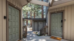 A wooden porch with two doors, a wooden staircase, and a view of a building in the background.