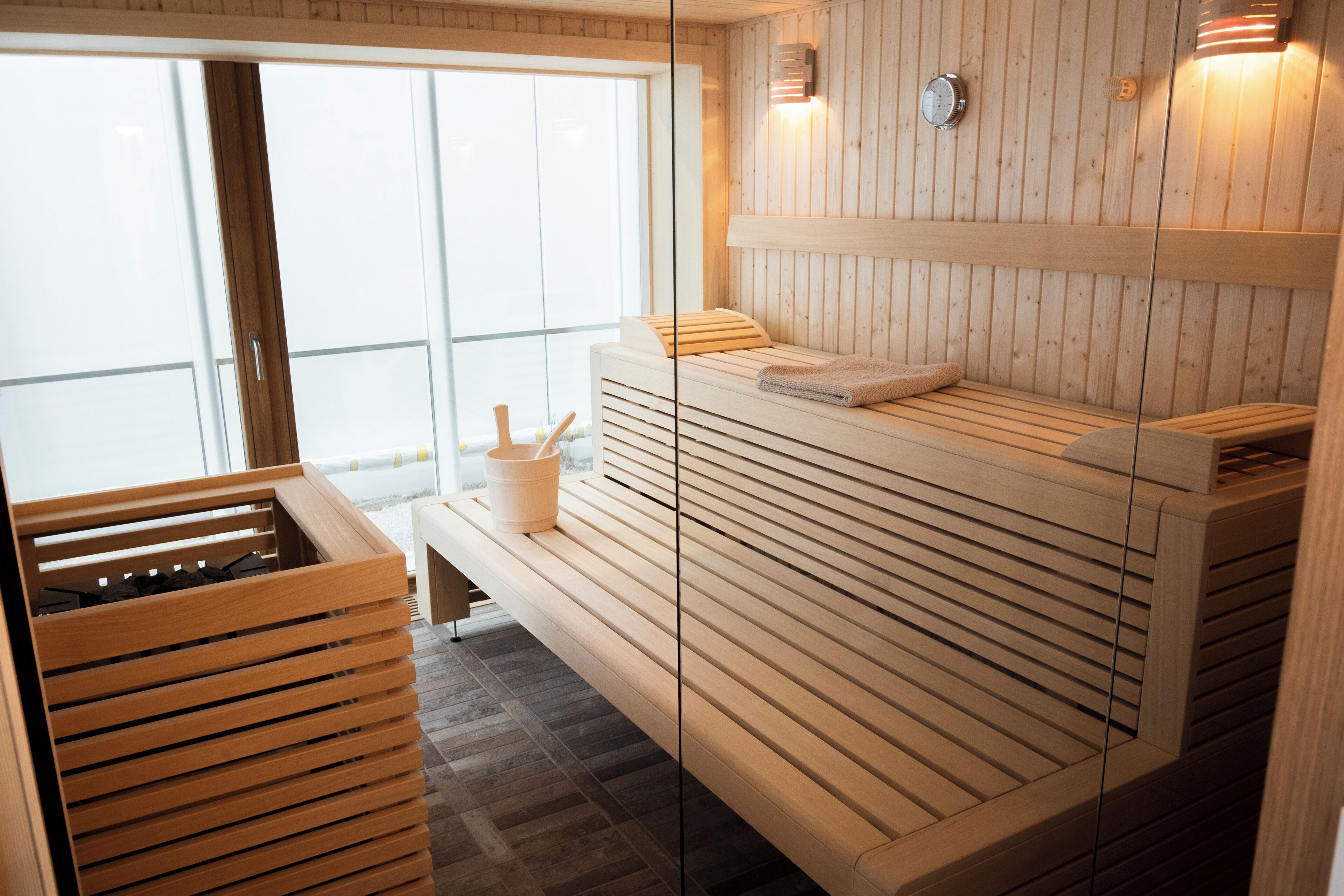 Un sauna avec des bancs en bois, un seau et une horloge fixée au mur.