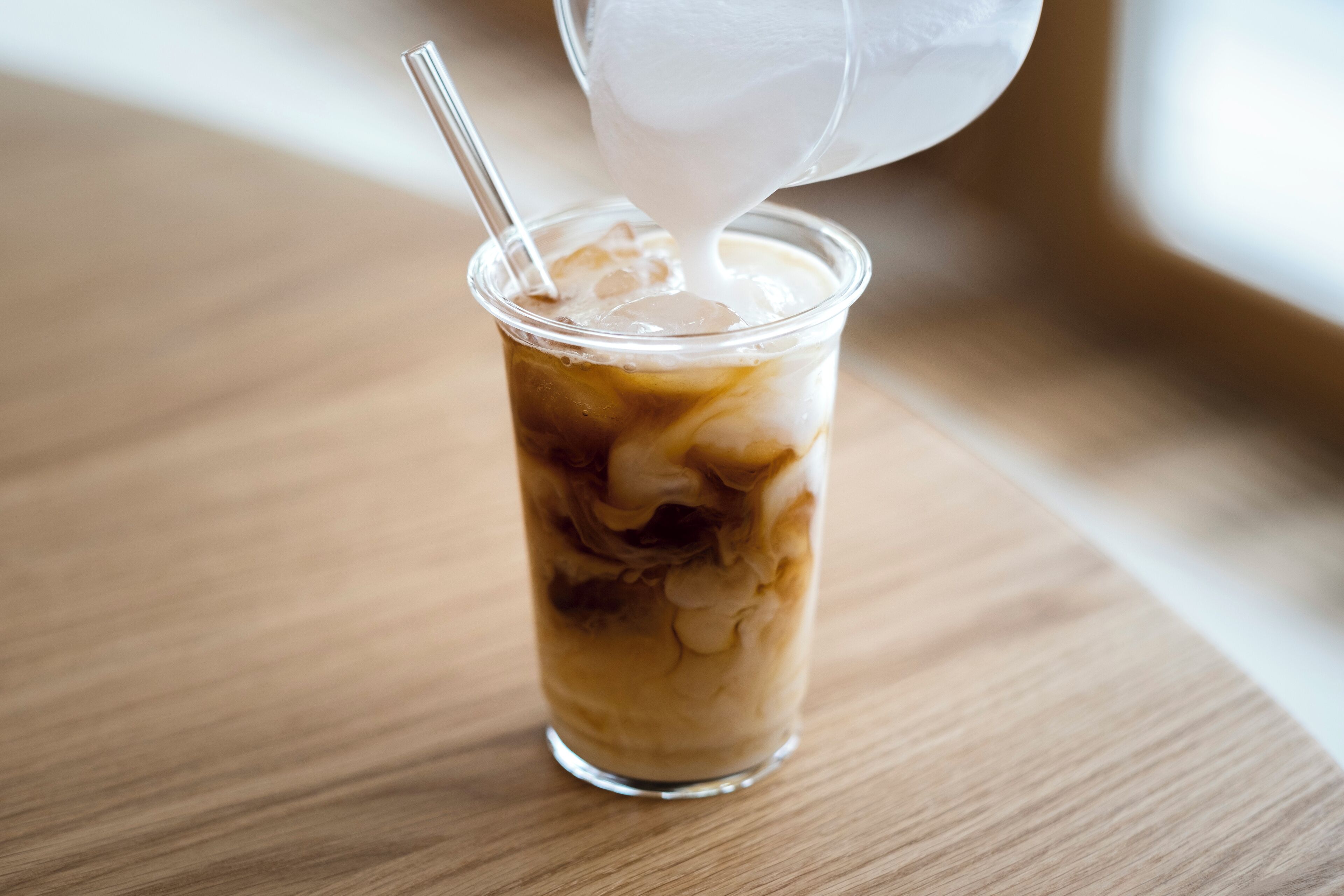 A clear glass cup with ice cubes and a straw, placed on a wooden surface.