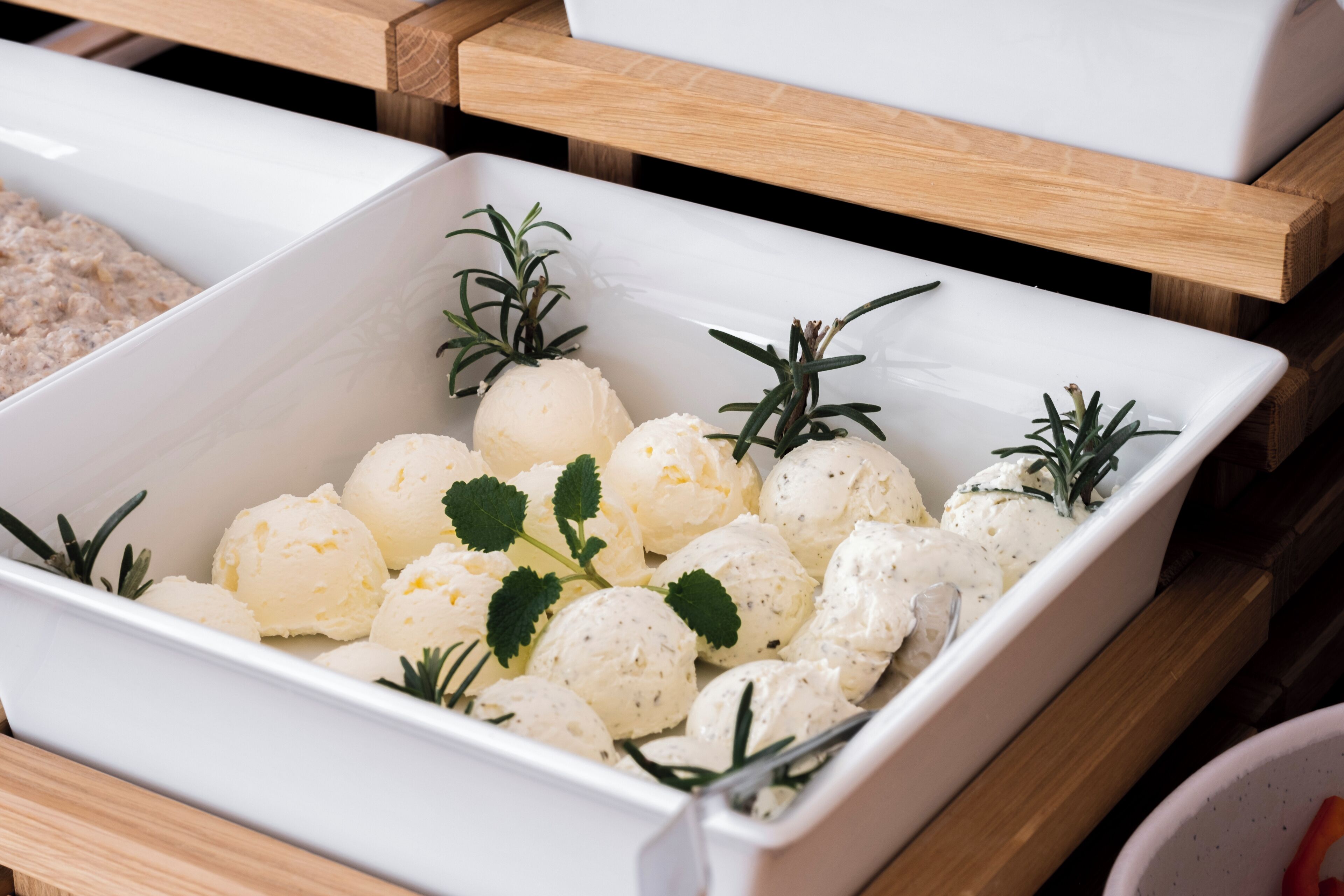 A white rectangular dish with white spherical food items garnished with rosemary sprigs, placed on a wooden surface.