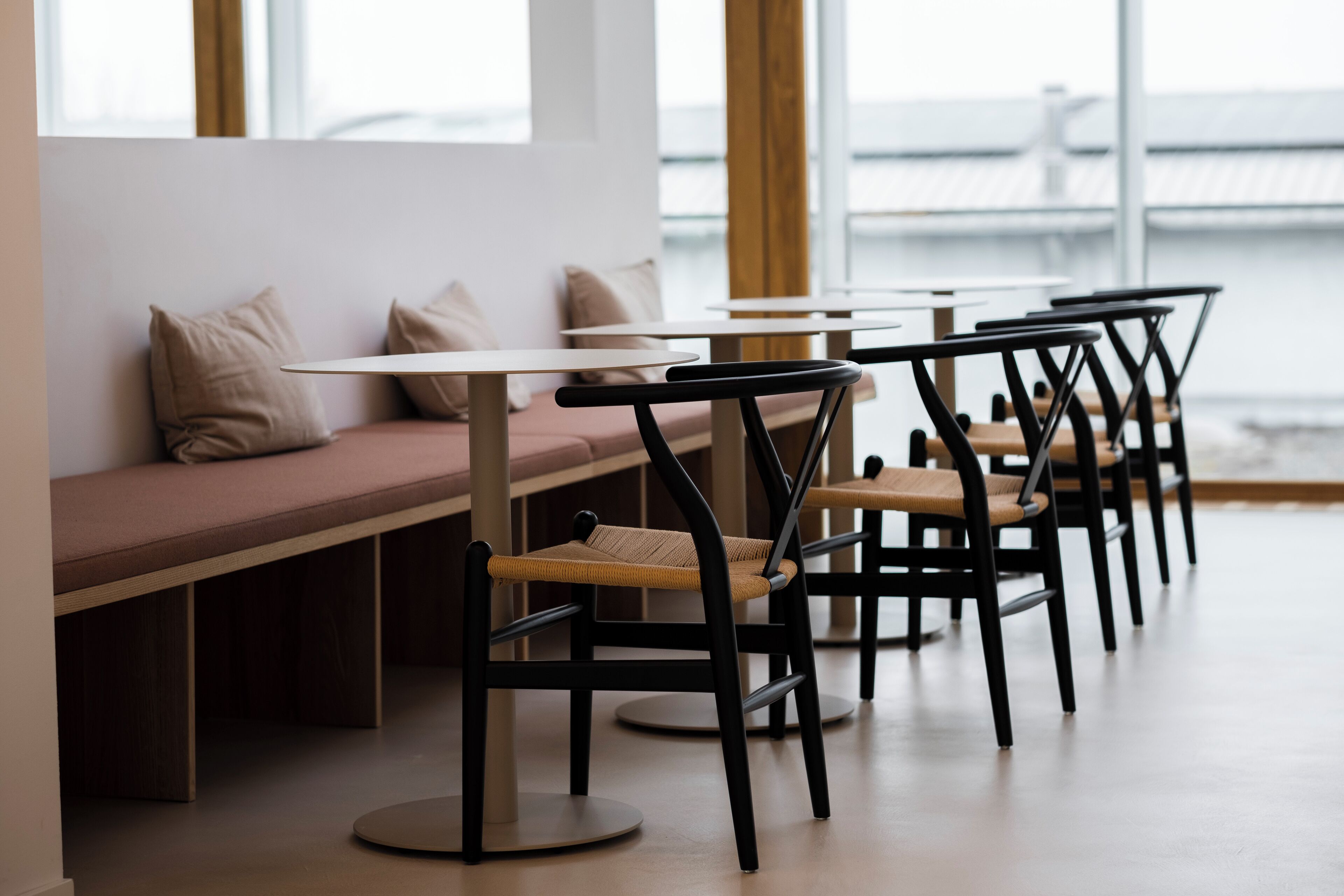A modern seating area with round tables and chairs, a bench with cushions, and large windows offering a view.