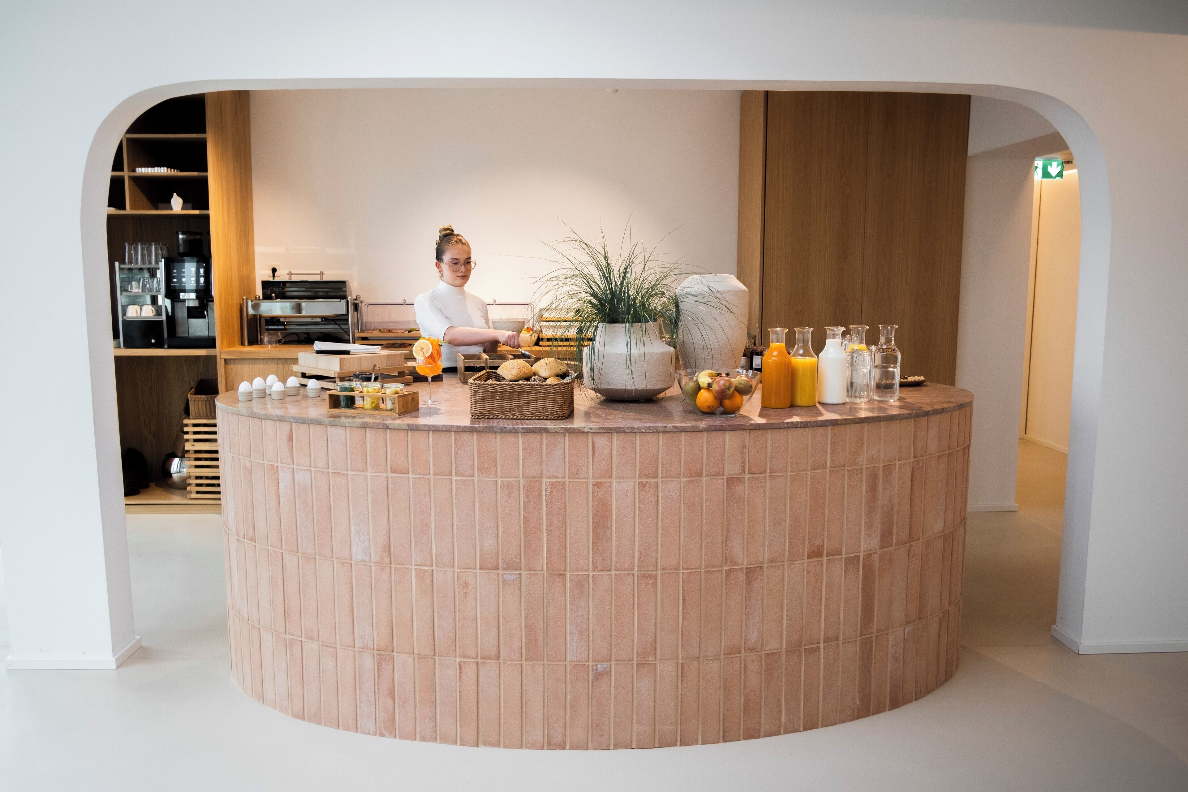 A breakfast bar with a variety of fruits, a coffee machine, and a potted plant.