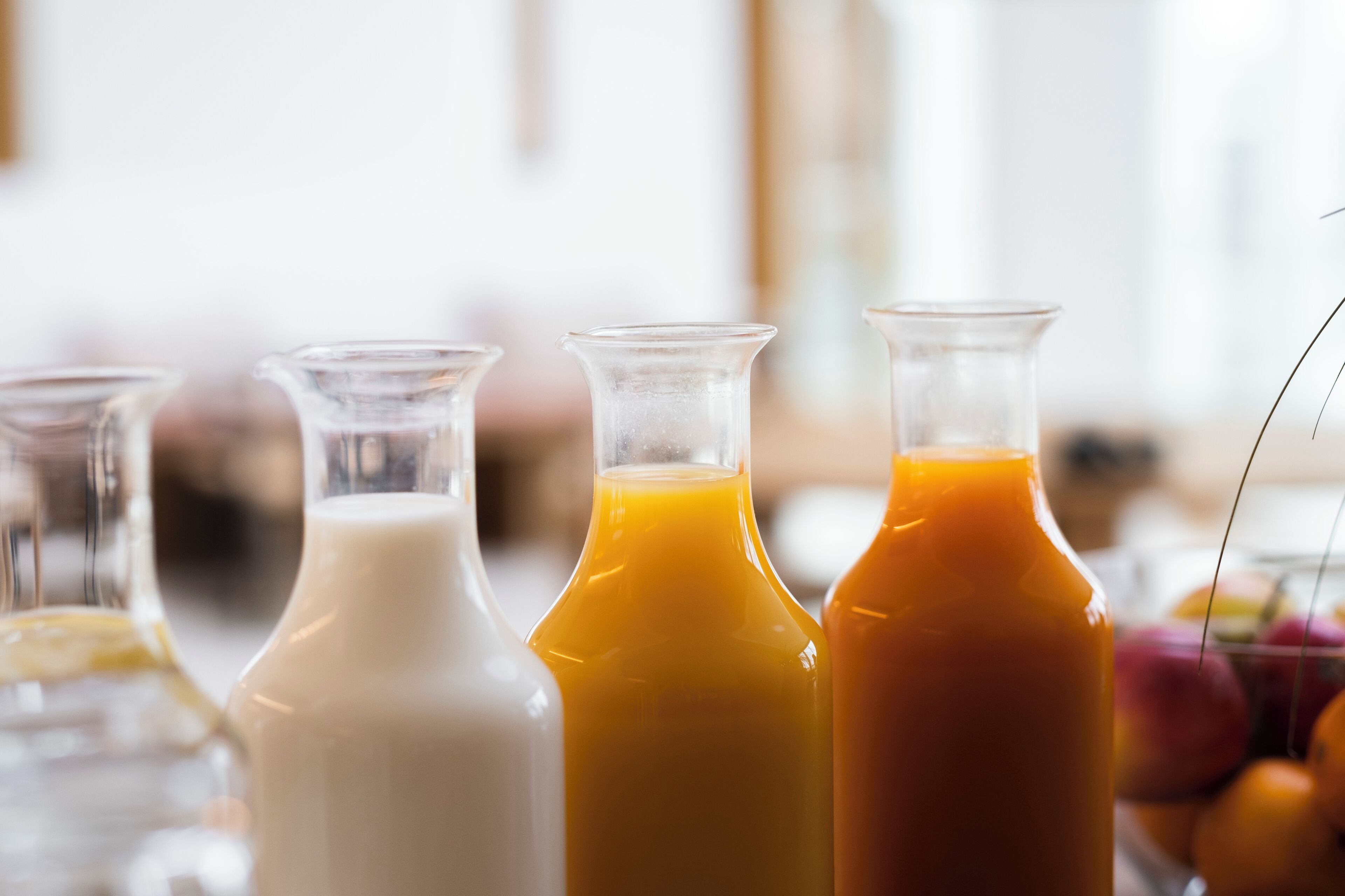 Fyra glasflaskor med olika färgade vätskor, troligen juicer eller smoothies, står på ett bord.