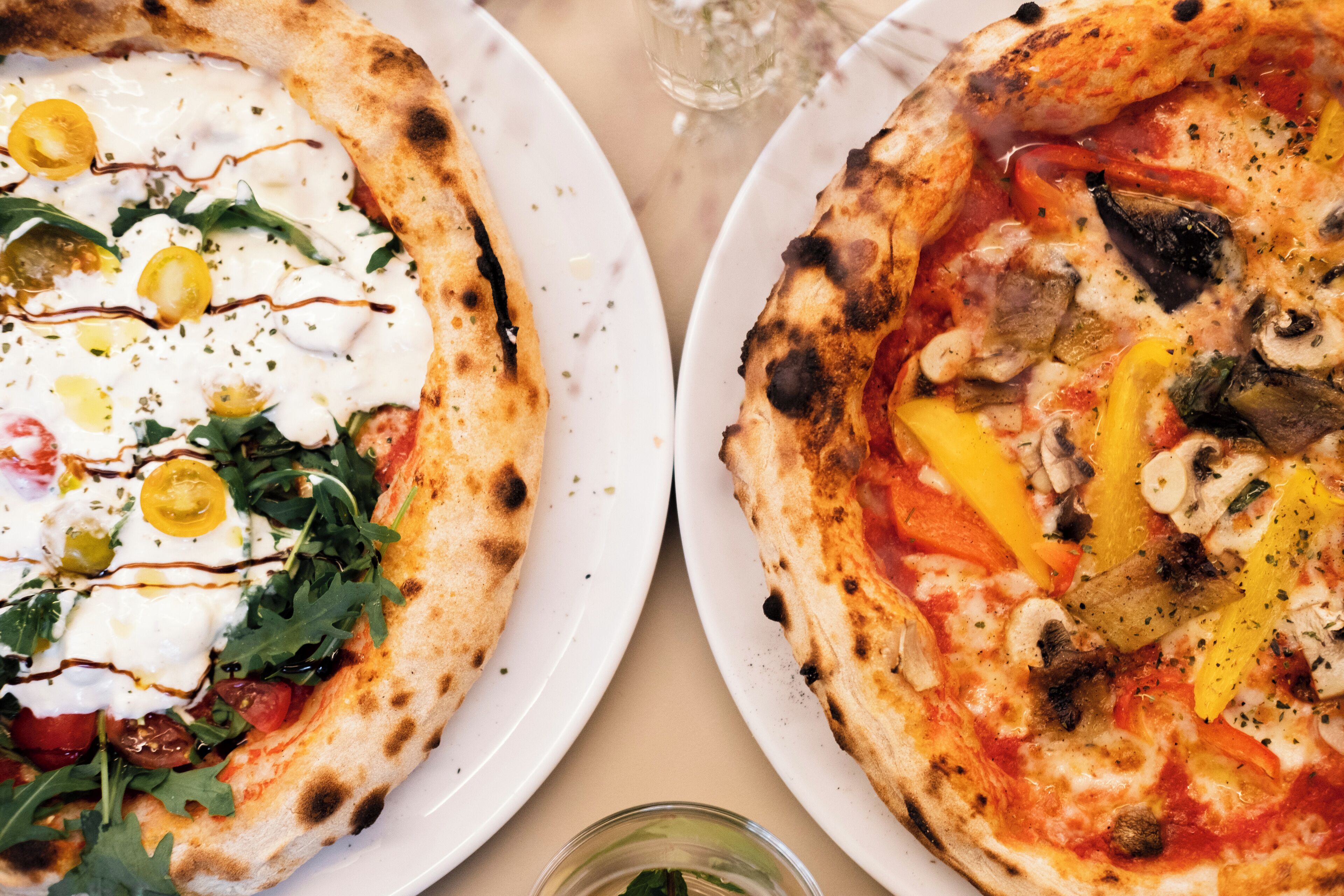 Two pizzas on white plates with various toppings.