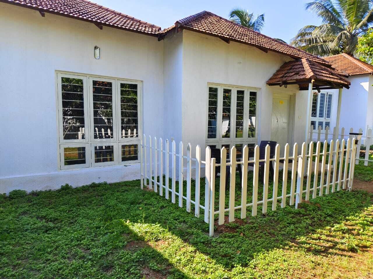 A white building with a tiled roof, a white picket fence, and a well-maintained lawn.