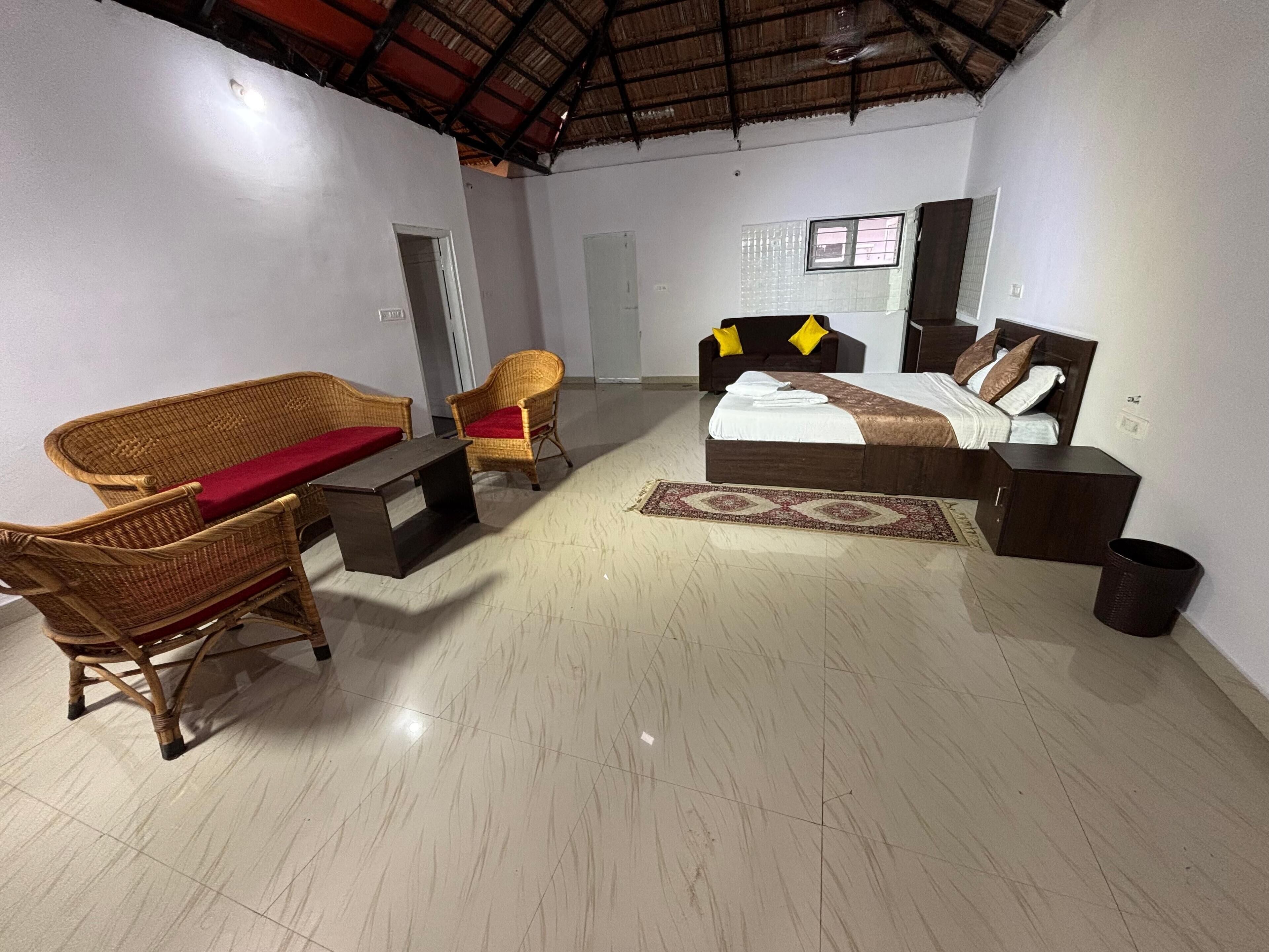 A spacious room with a bed, two wicker chairs, a small table, and a tiled floor.